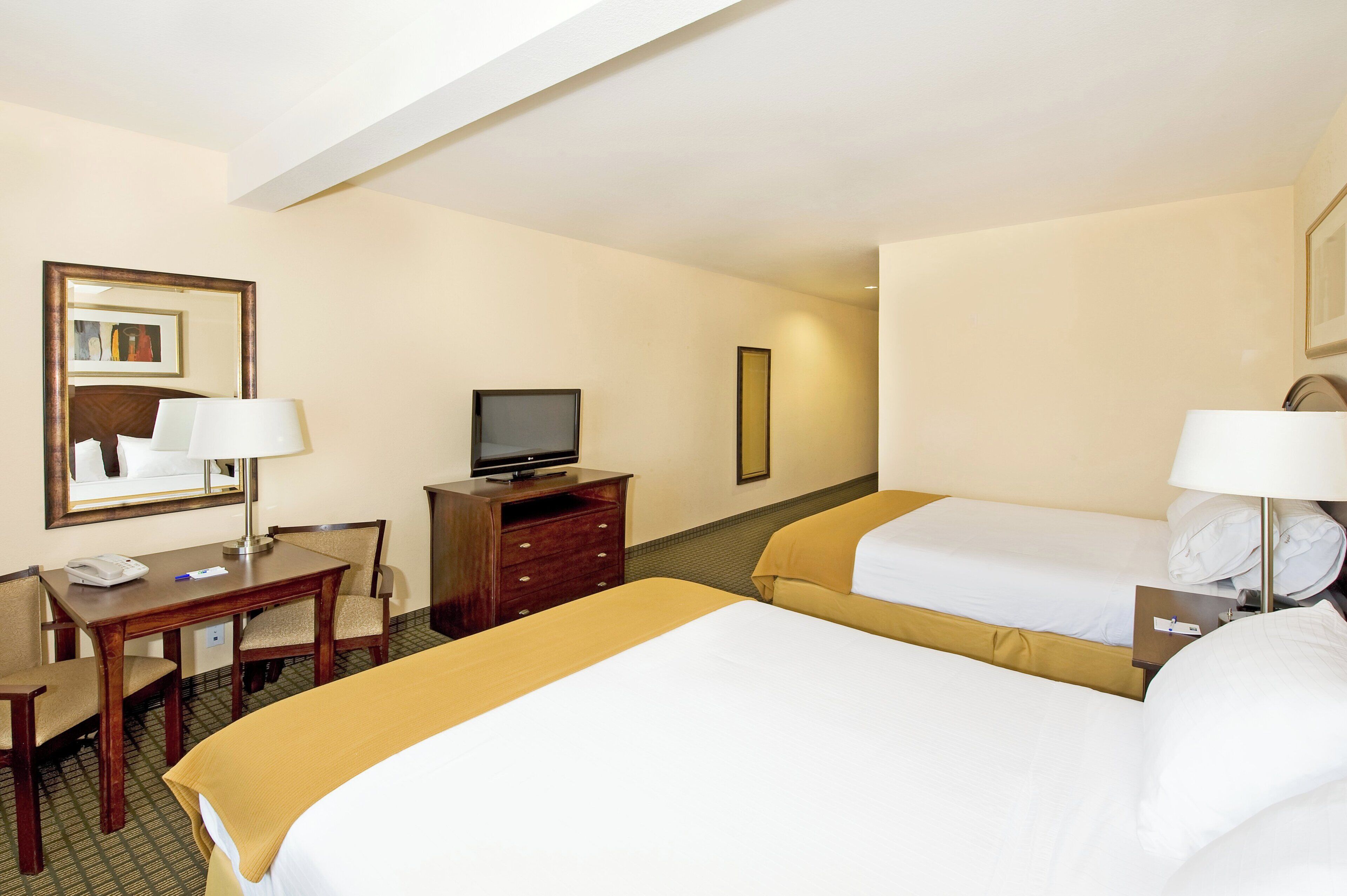 A hotel room with two beds, a desk, a television, and a mirror.