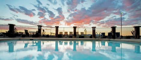 Una piscina con vista al atardecer, rodeada por una cerca y sillones de descanso.