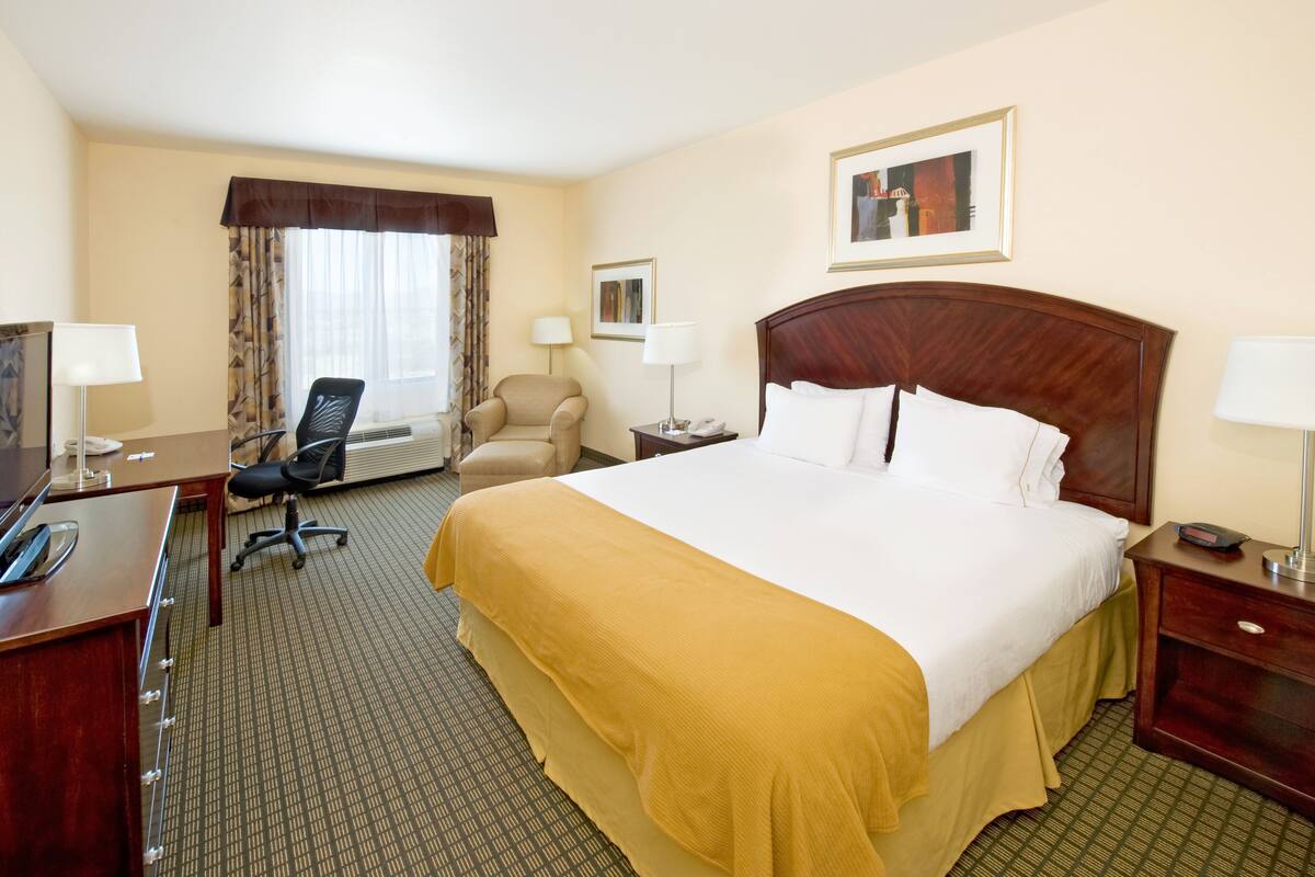 A hotel room with a large bed, a desk with a telephone, a chair, and a window with curtains.