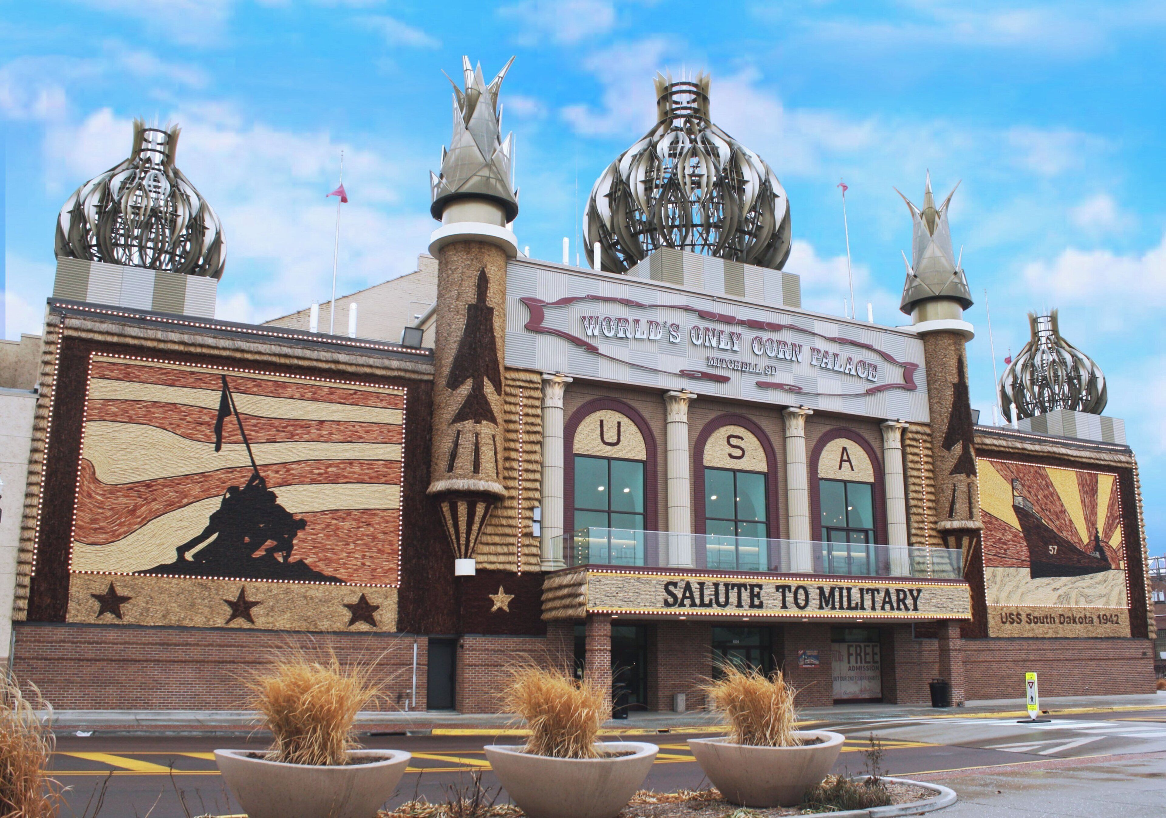 A building with a large mural depicting a military scene, a sign reading 'WORLD'S ONLY CORN PALACE,' and a 'SALUTE TO MILITARY' sign.