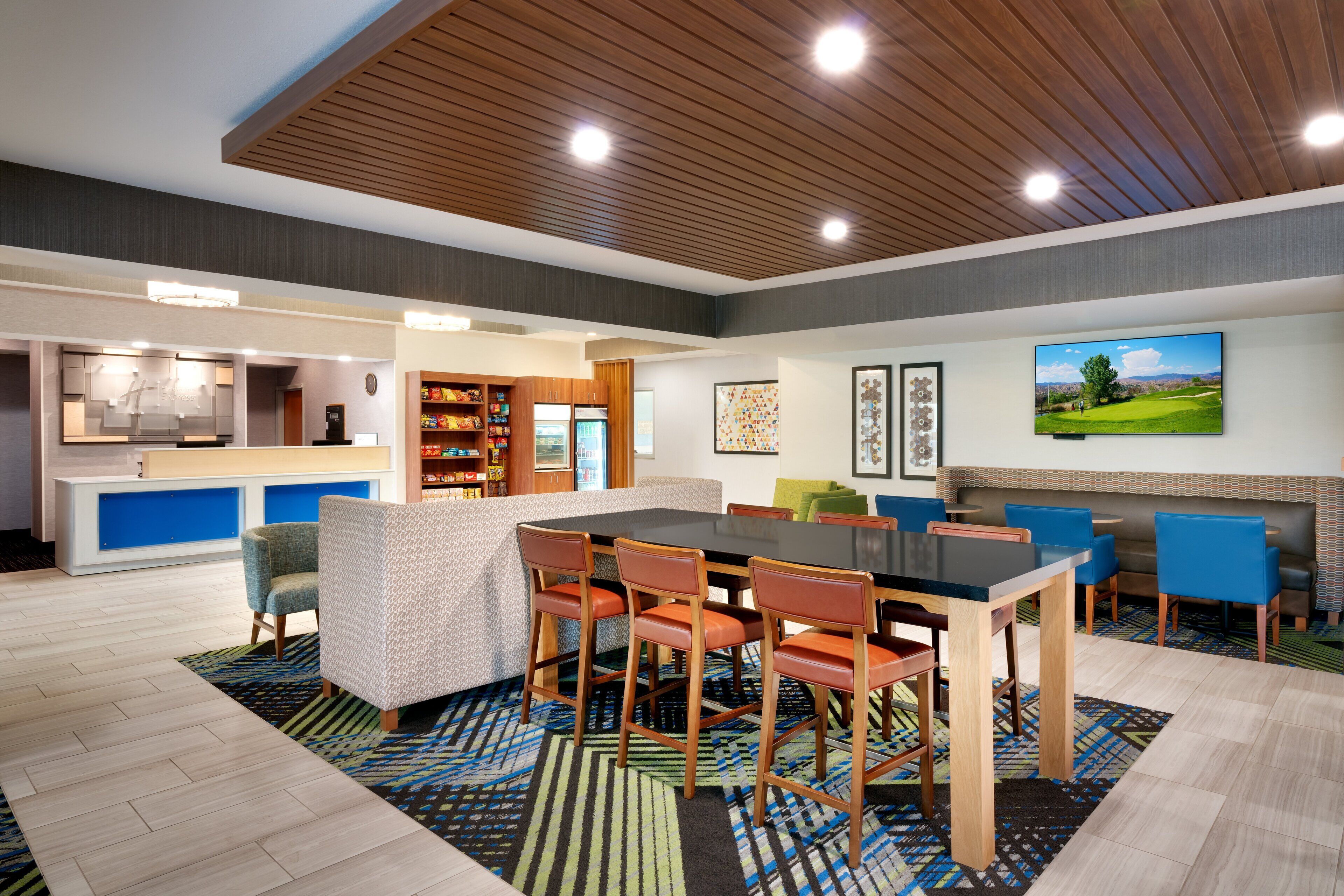 Un moderno vestíbulo de hotel con zona de comedor, cocina y una televisión mostrando un campo de golf.