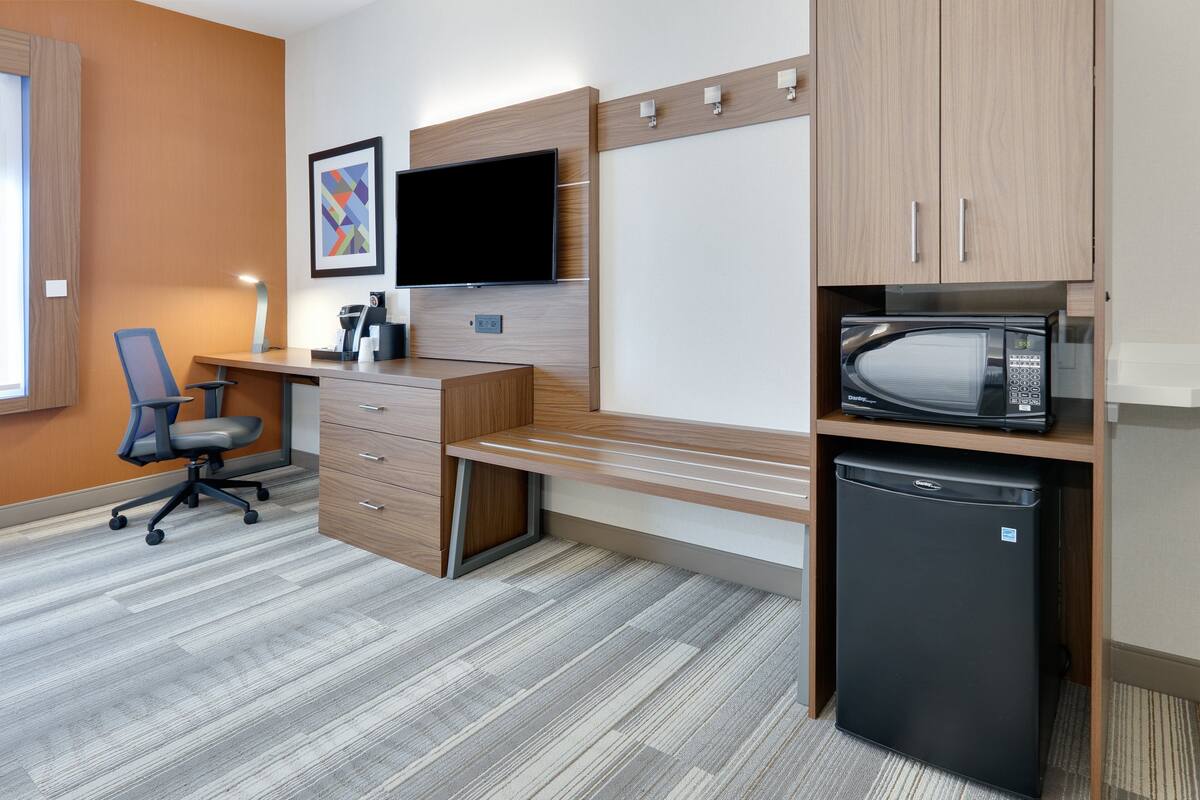 A modern office space with a desk, chair, television, microwave, and refrigerator.