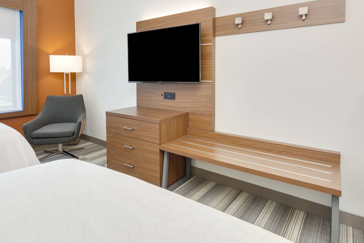 A hotel room with a bed, a desk with a flat-screen TV, a chair, and a lamp.