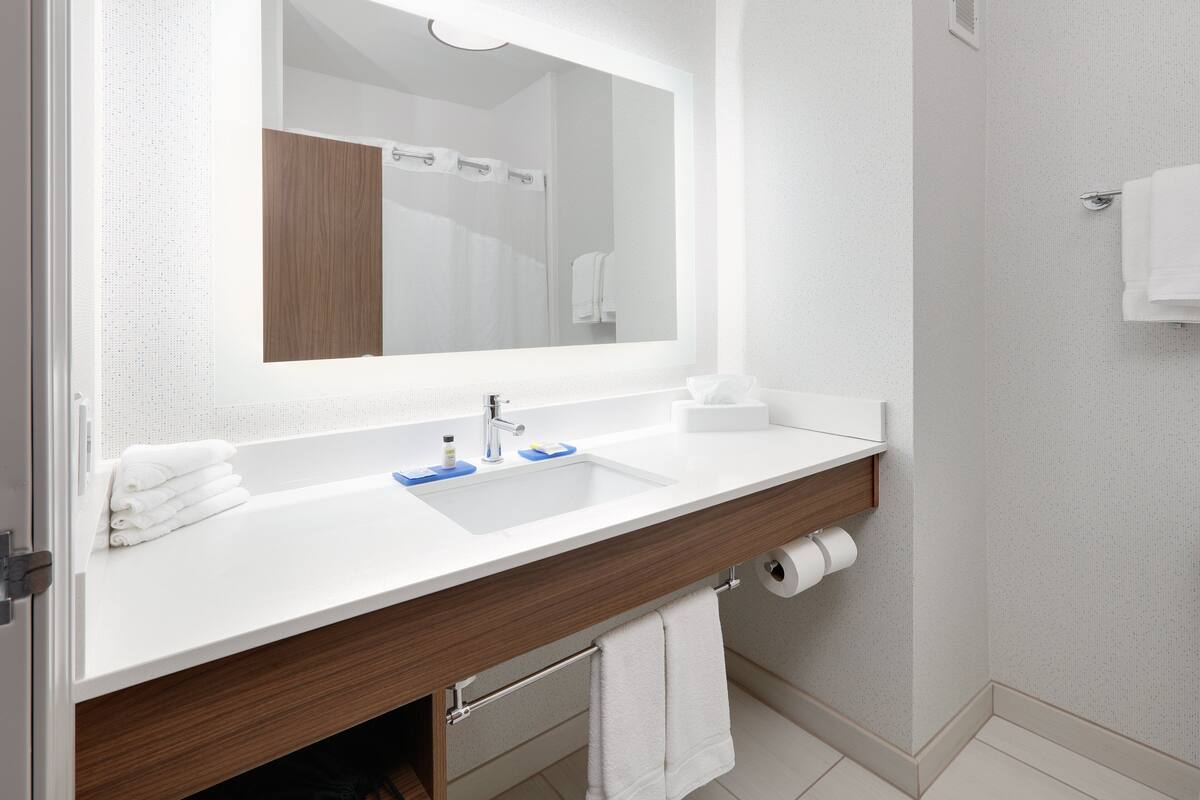 A modern bathroom with a white sink, wooden vanity, and a large mirror.