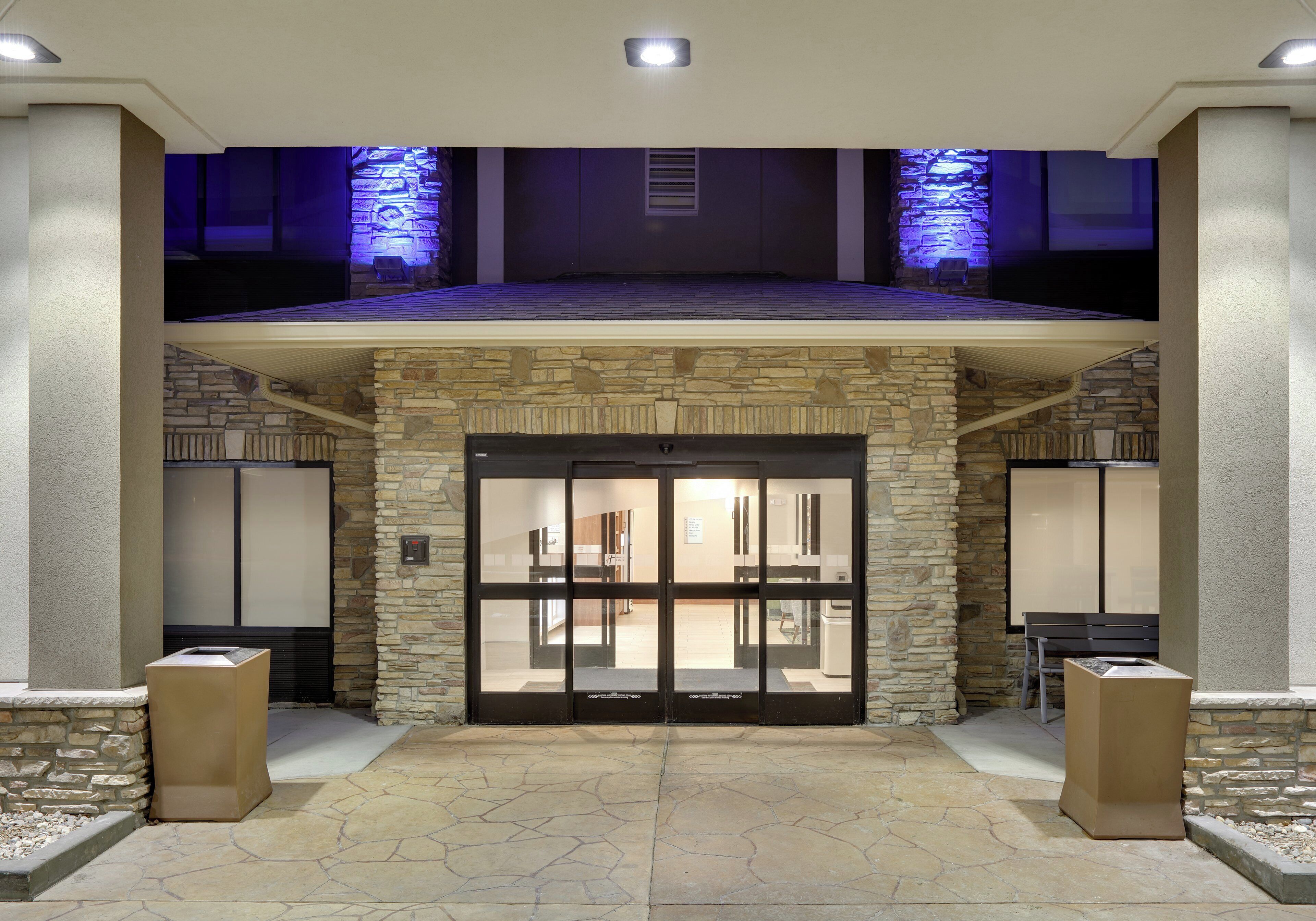 Fachada de hotel de piedra, puerta de cristal y un nivel superior cubierto con iluminación azul.