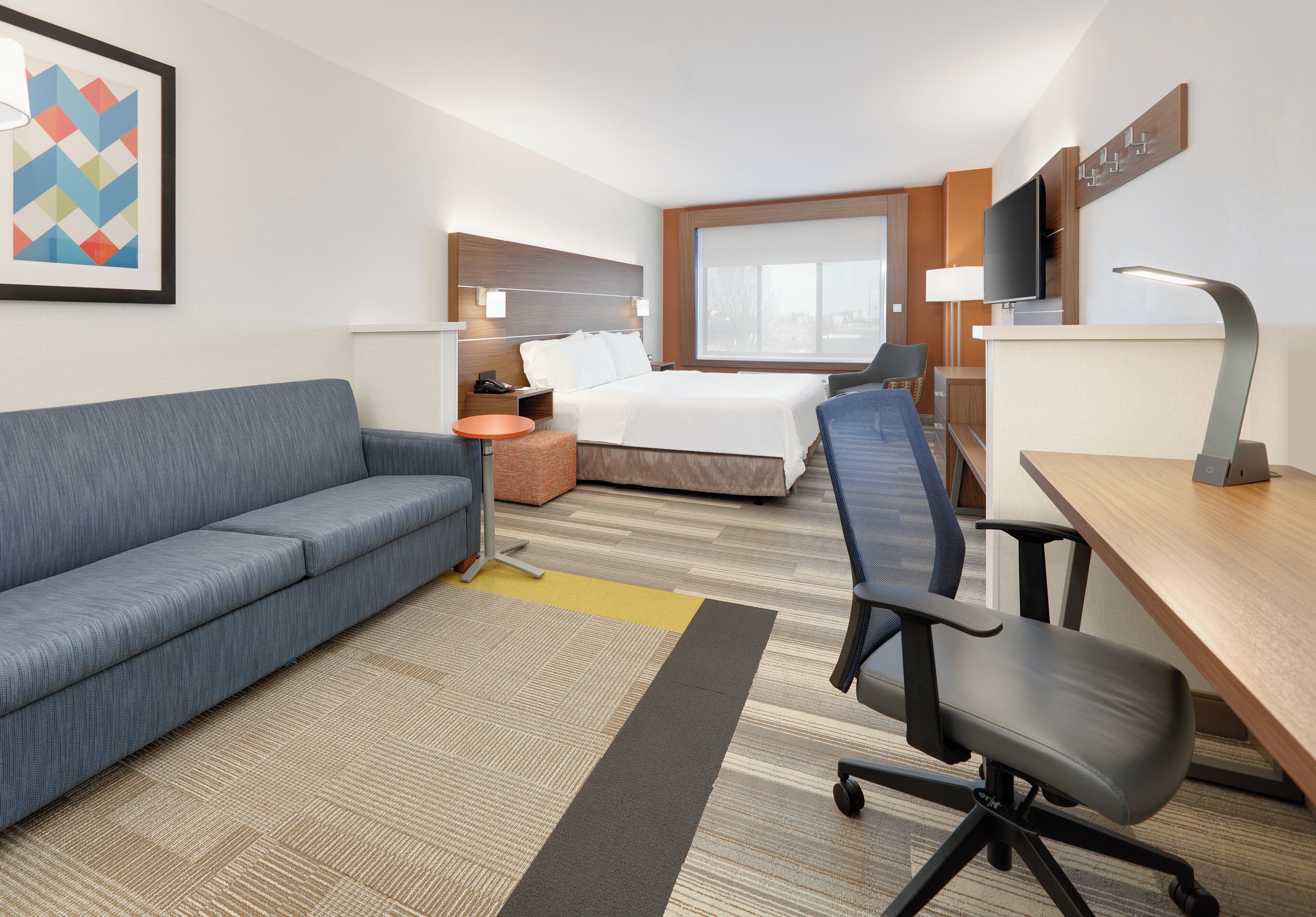 A hotel room with a bed, a sofa, a desk, and a TV.