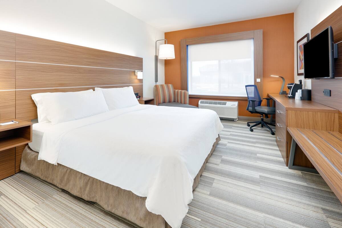 A hotel room with a large bed, a desk, a chair, a TV, and a window.