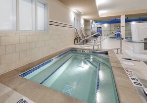 An indoor swimming pool with clear water, a tiled deck, and a lifeguard chair.
