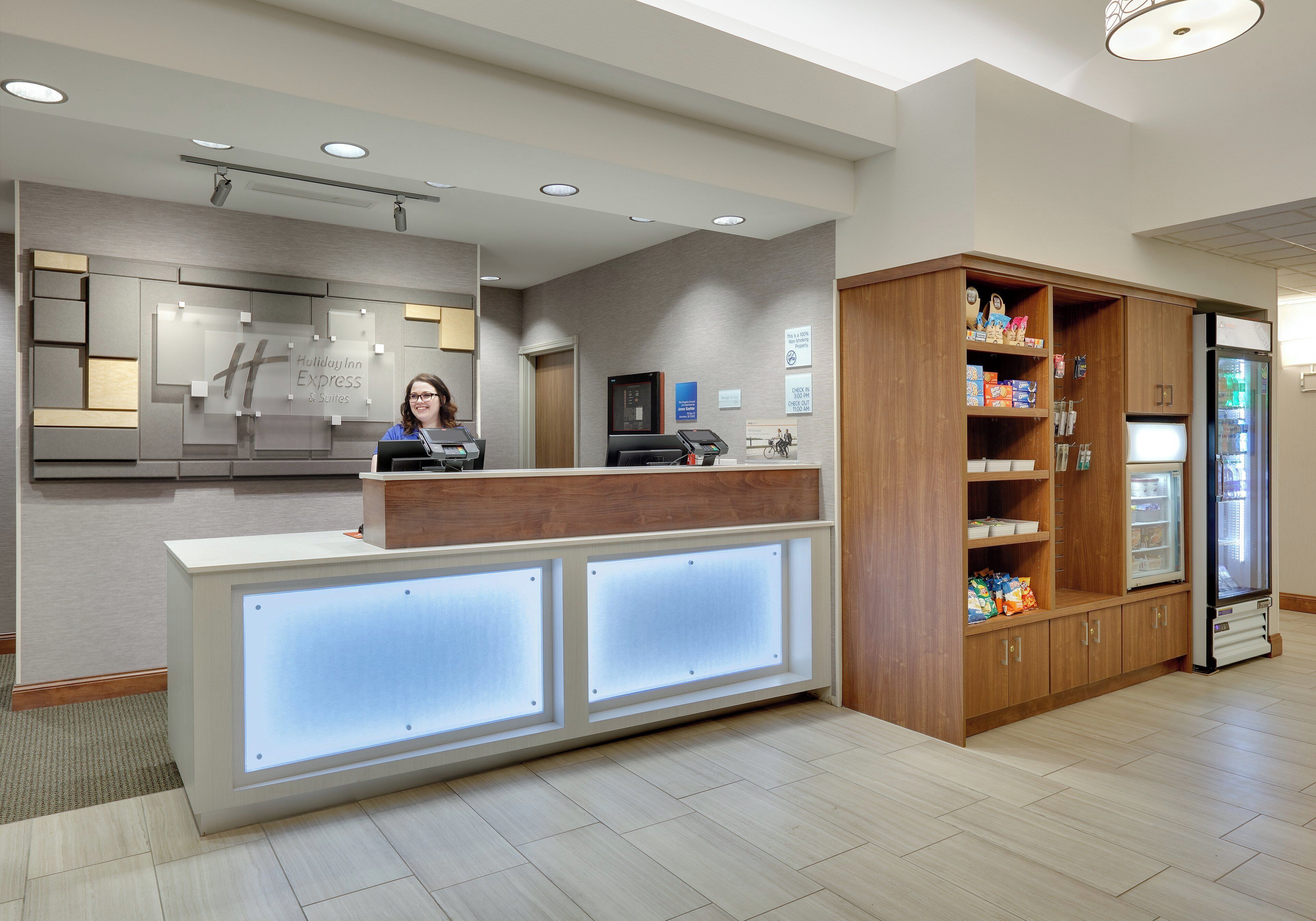 A hotel reception area with a reception desk, a digital display, a vending machine, and a wooden cabinet with snacks.