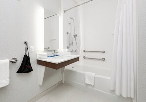 A modern bathroom with a white sink, mirror, and bathtub. There is a towel rack with a black bag hanging on it.