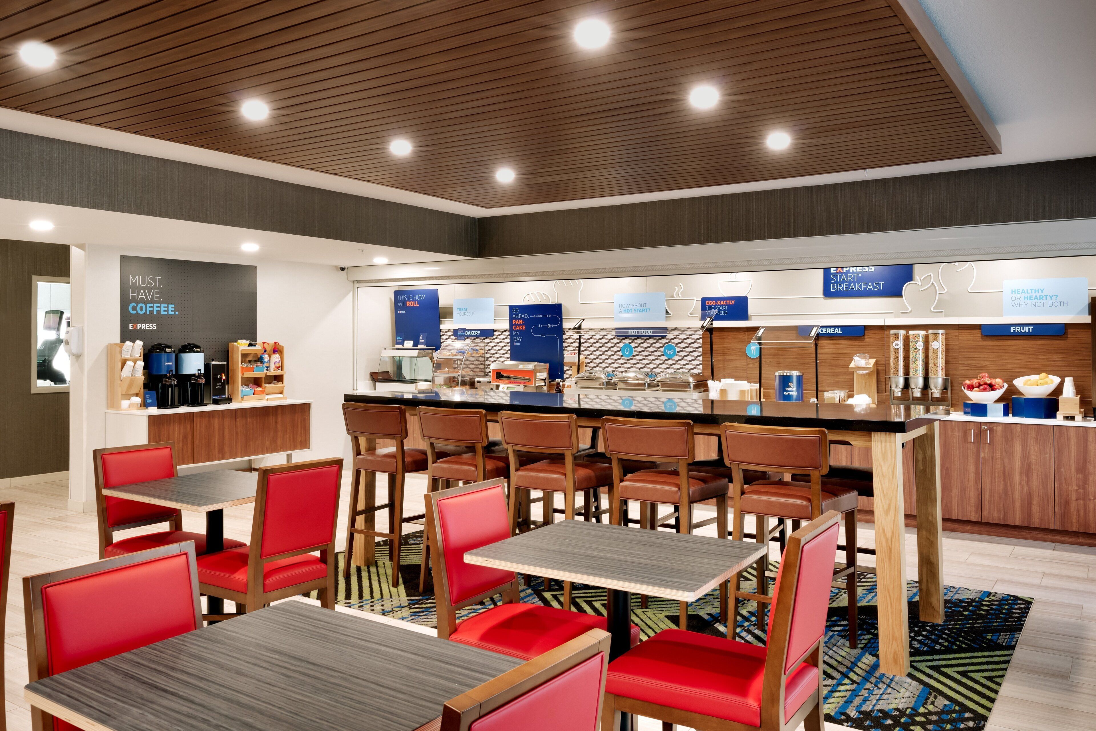 A modern cafe with red and brown chairs, a coffee bar, and a breakfast counter.