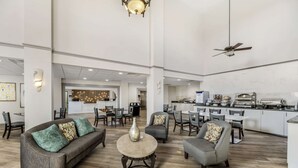 A spacious lobby with a sofa, chairs, a coffee table, a ceiling fan, and a kitchen area in the background.