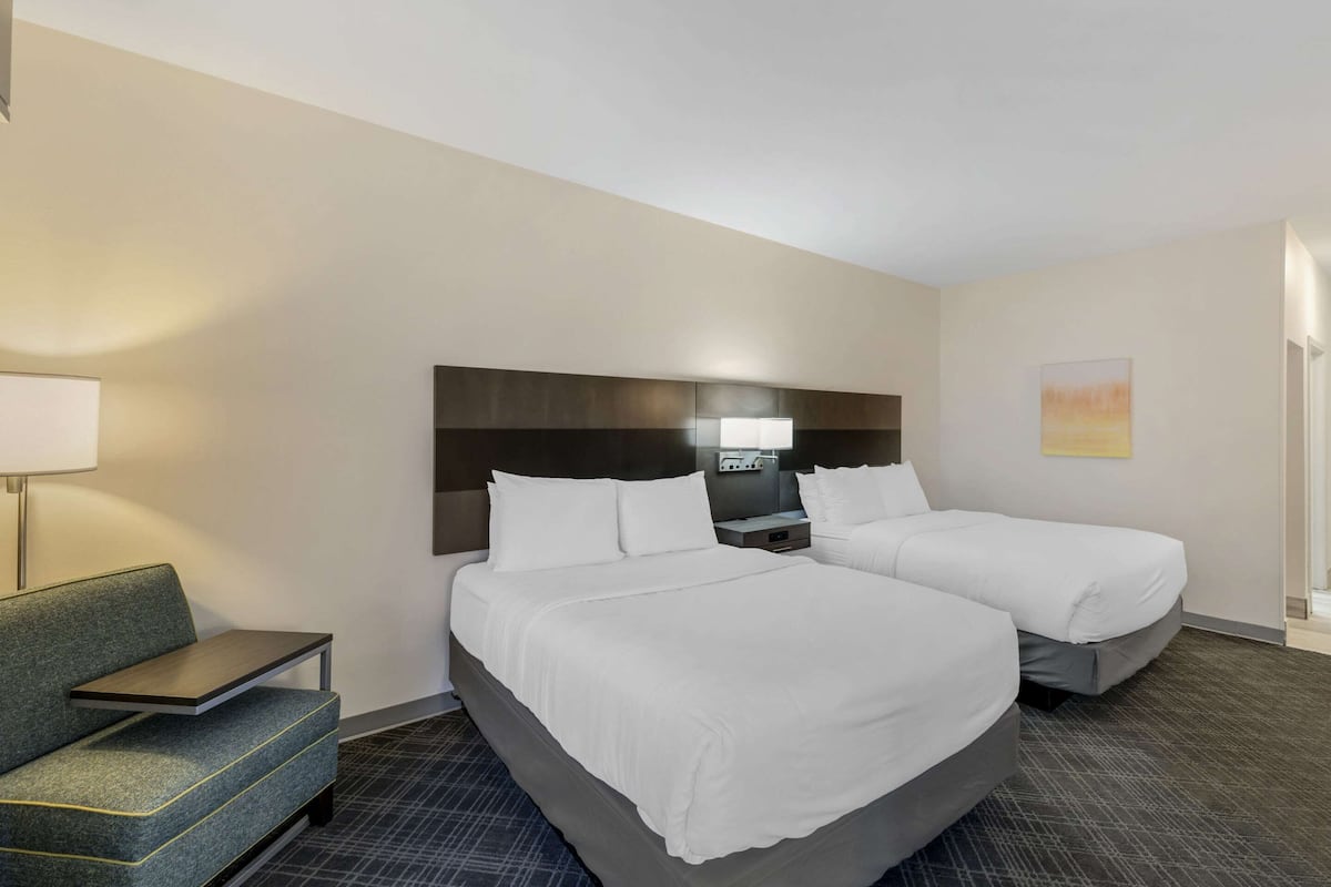 Een hotelkamer met twee bedden, een bank, een nachtkastje en een lamp.