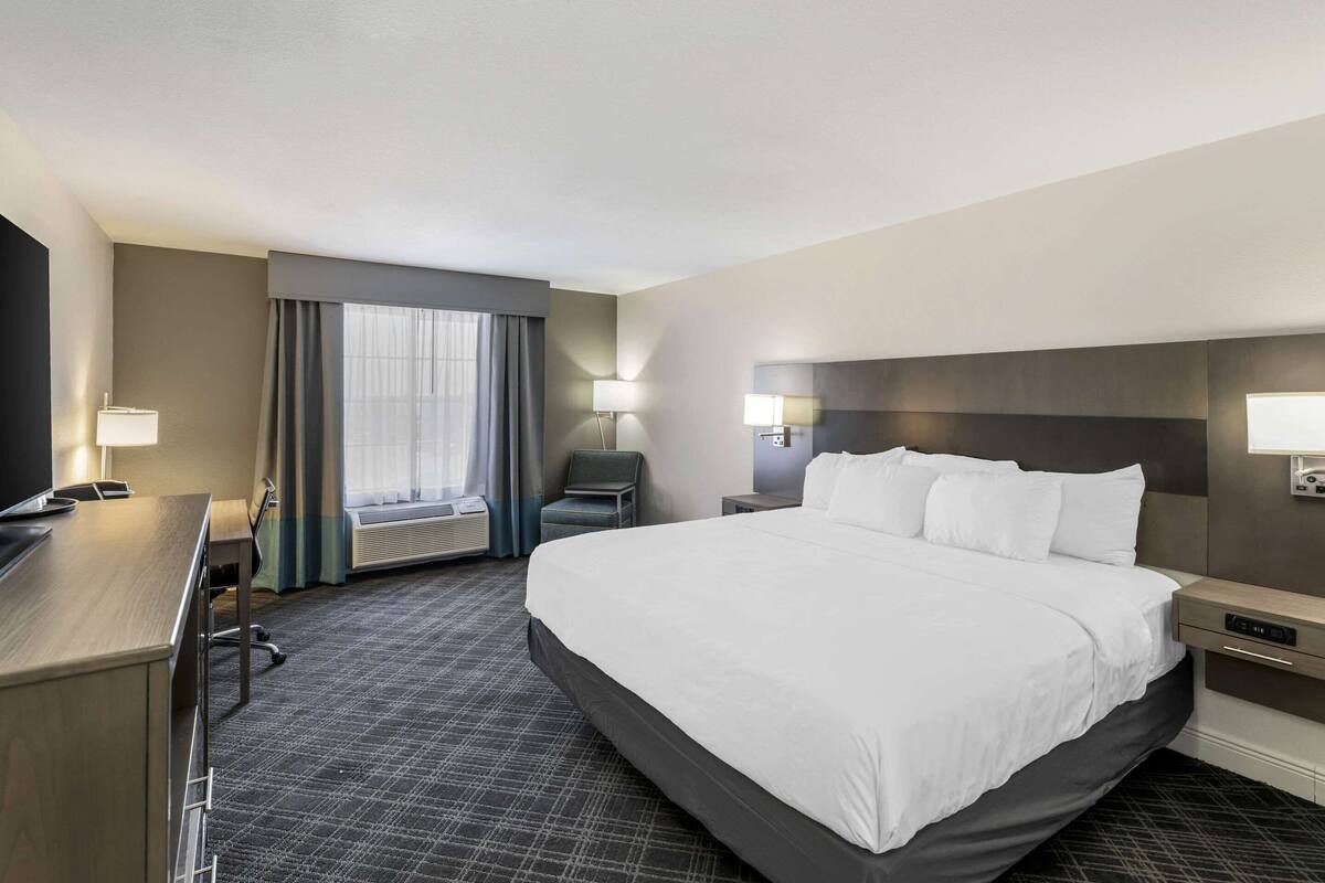 Hotelkamer met een groot bed, een bureau, een stoel, een televisie, een lamp en een raam met gordijnen.