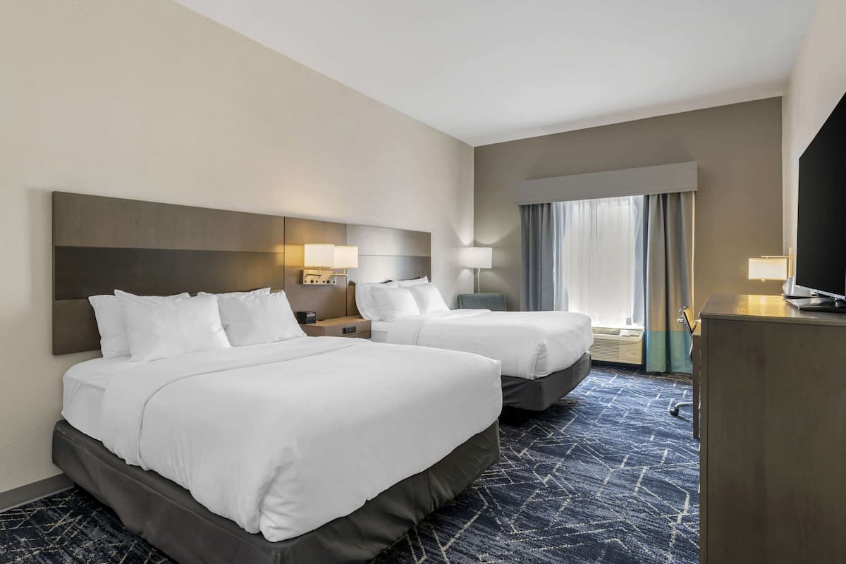 Een hotelkamer met twee bedden, een groot hoofdeinde, bedlampen, een flatscreen televisie en een groot raam met gordijnen.