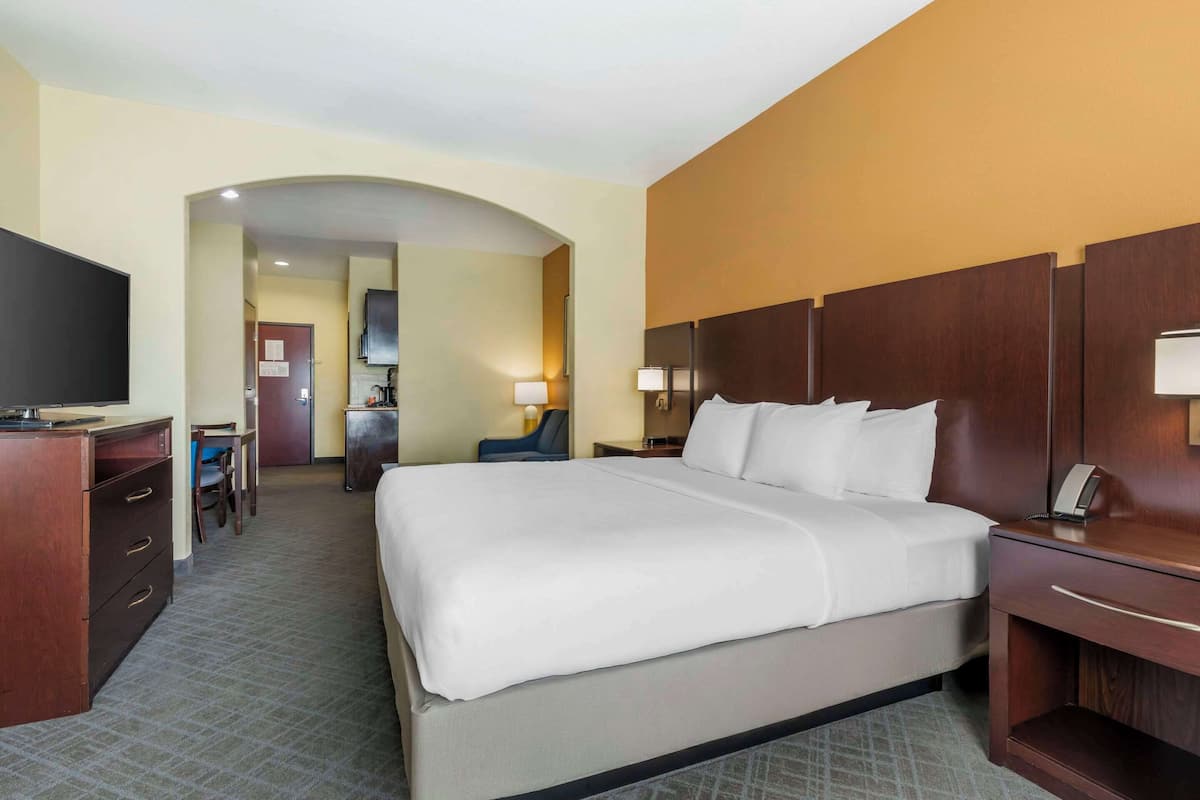 A hotel room with a large bed, a desk with a chair, a TV, and a bathroom visible through an archway.
