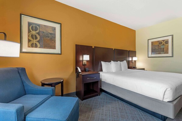 A hotel room with a bed, a sofa, a nightstand with a lamp, and two framed artworks on the walls.