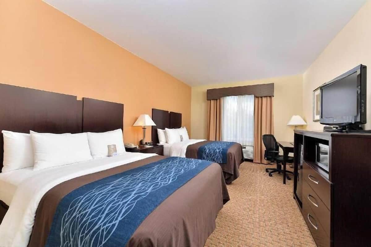 A hotel room with two beds, a desk, a television, and a window with curtains.
