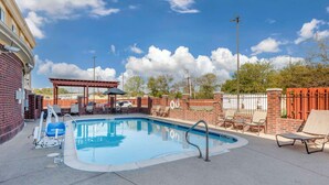 A swimming pool with lounge chairs, a covered seating area, and a brick wall.