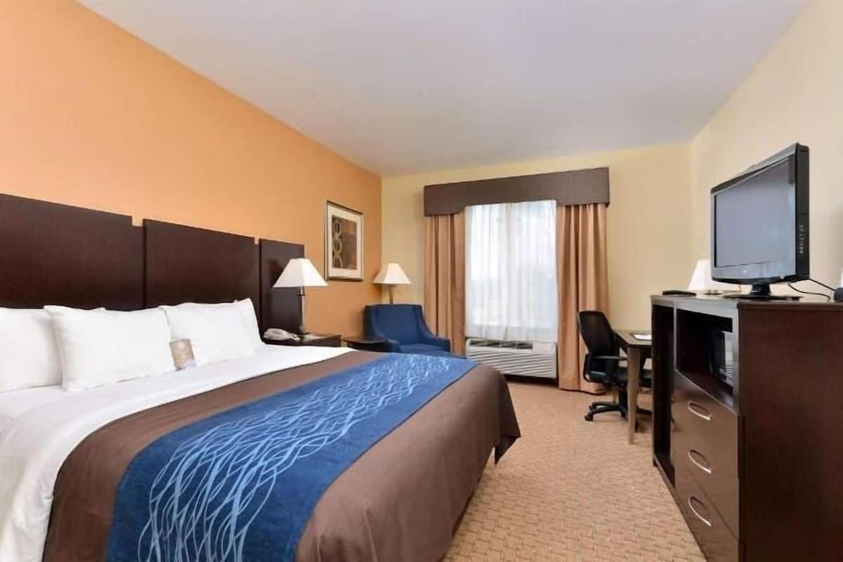 A hotel room with a large bed, a desk with a computer, a chair, a television, and a window with curtains.