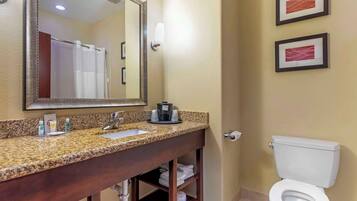 A bathroom with a granite countertop sink, a mirror, a toilet, and two framed pictures on the wall.