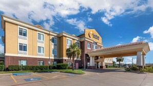 A hotel with a yellow facade, a covered parking area, and a clear blue sky.