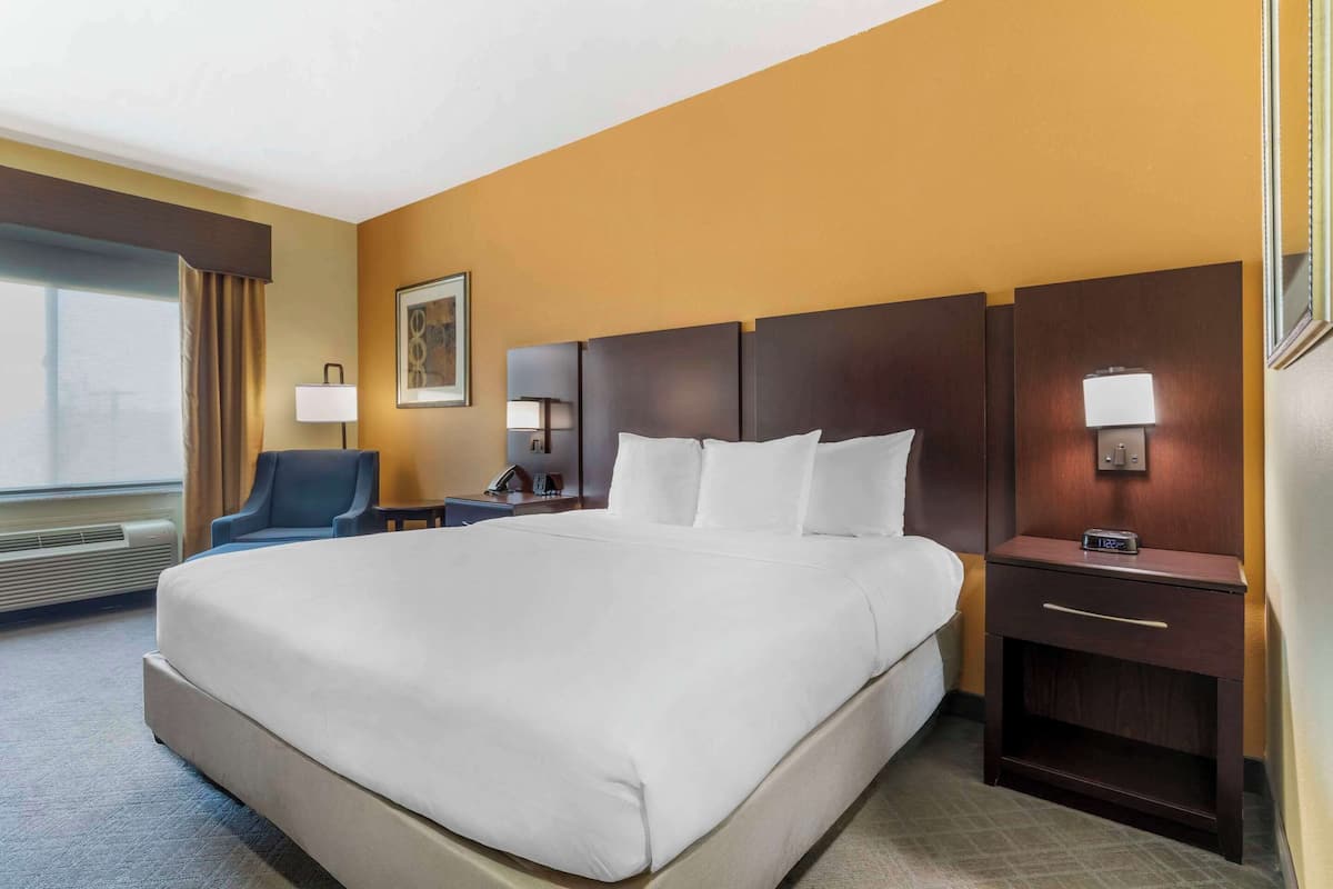 A hotel room with a large bed, a desk with a lamp, a chair, and a window with curtains.