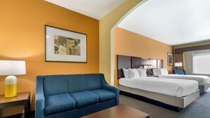 A hotel room with a blue sofa, a bed with white bedding, a bedside table with a lamp, and a framed picture on the wall.