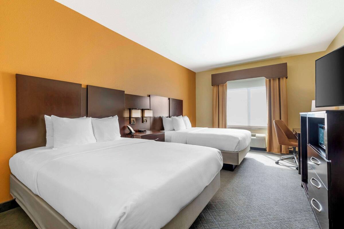 A hotel room with two beds, a desk, a chair, a television, and a large window with curtains.