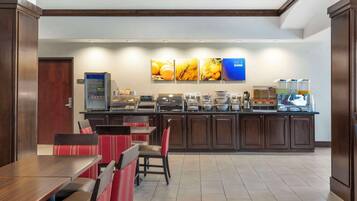 A breakfast bar with various food options and a coffee station. There are seating areas with red and black chairs.