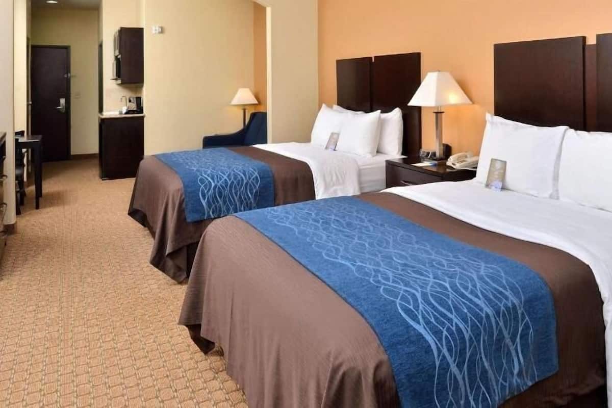 A hotel room with two beds, a nightstand, a lamp, a desk, and a wardrobe.