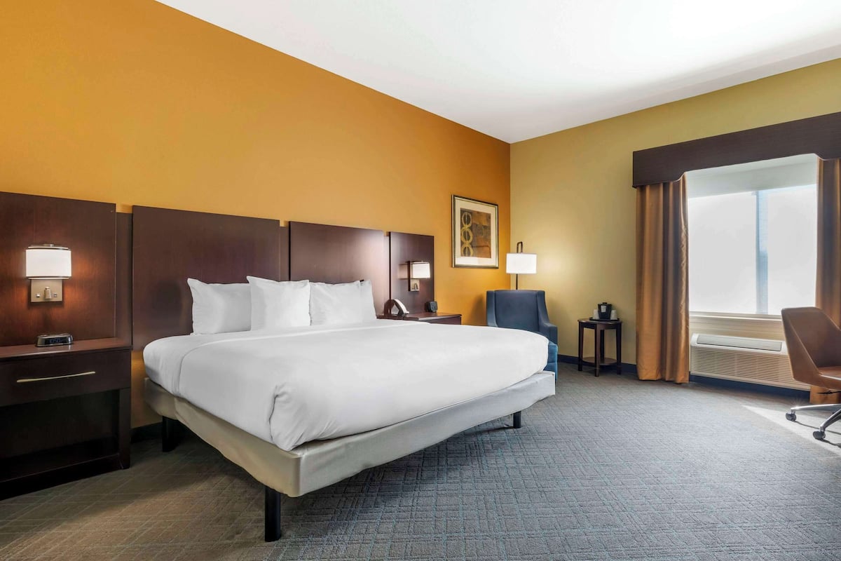 A hotel room with a large bed, bedside tables with lamps, a chair, a small table, and a window with curtains.
