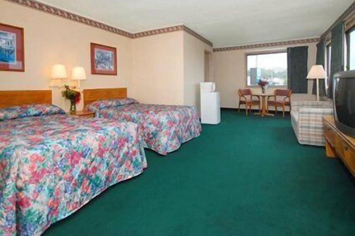 A hotel room with two beds, a small table, a chair, a TV, and a window.