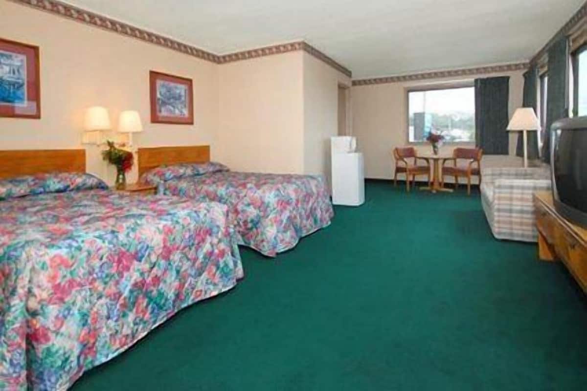 A hotel room with two beds, a small table, a chair, a TV, and a window.