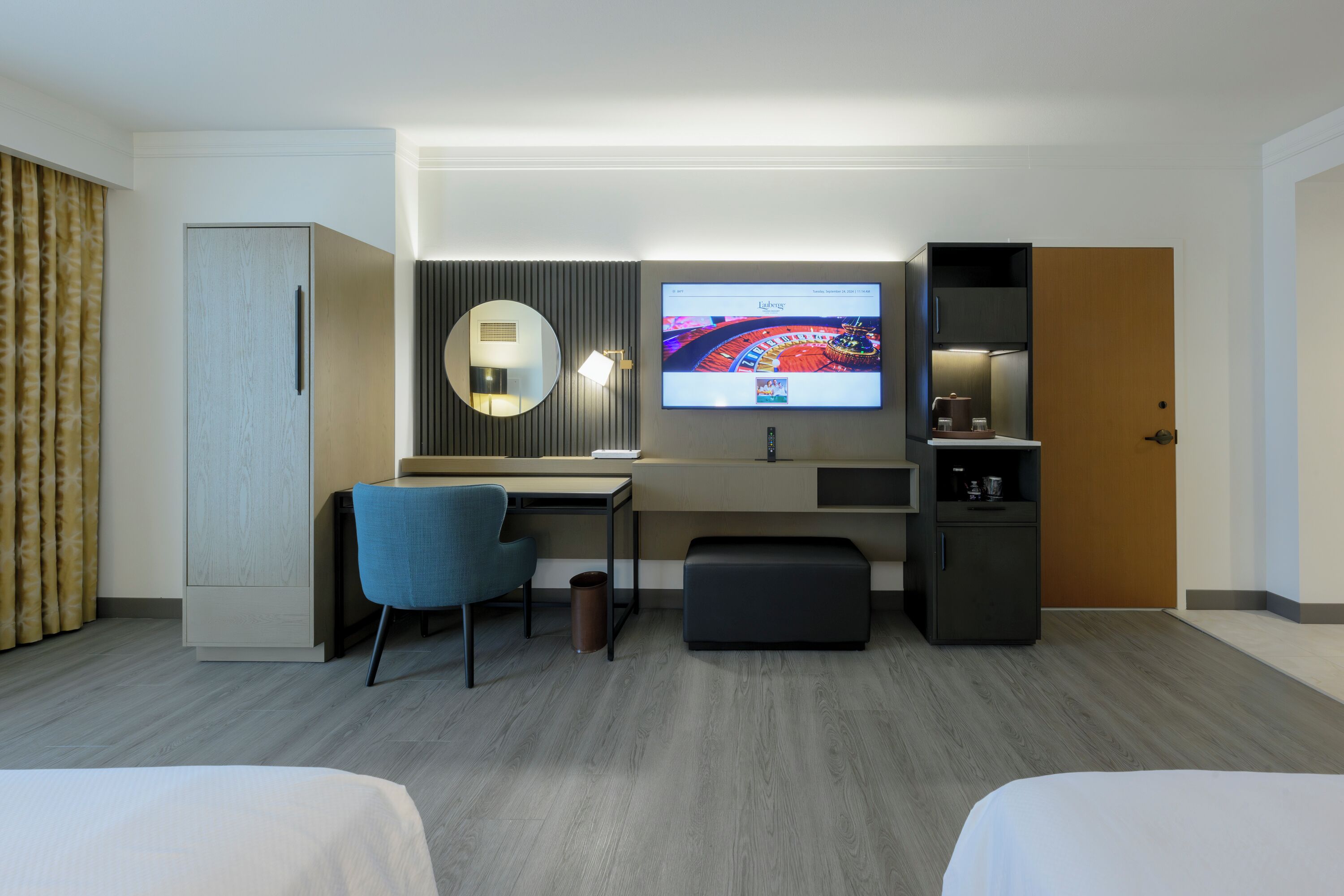 Habitación de hotel con cama, escritorio, silla, televisión, espejo, armario y minibar.