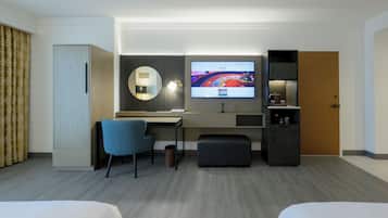 Habitación de hotel con cama, escritorio, silla, televisión, espejo, armario y minibar.