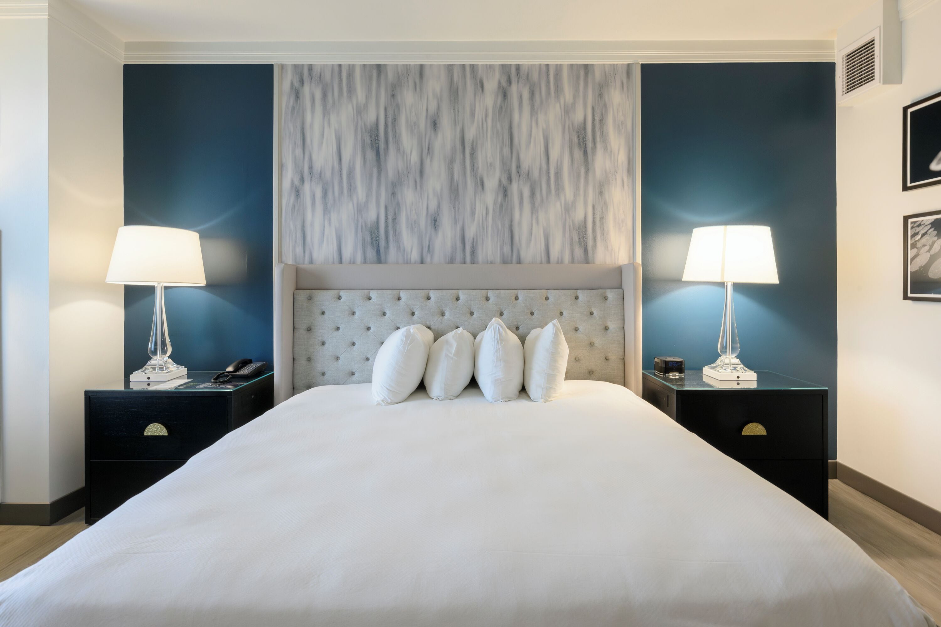 A hotel room with a large bed, two bedside tables, and a headboard with a textured design.