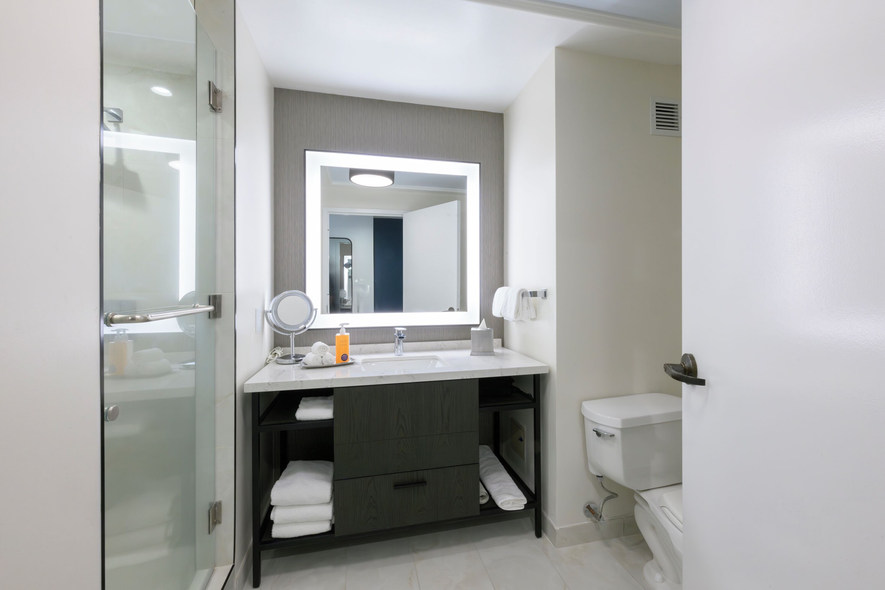 Un baño moderno con cabina de ducha de vidrio, un lavamanos blanco con un espejo grande y un inodoro.