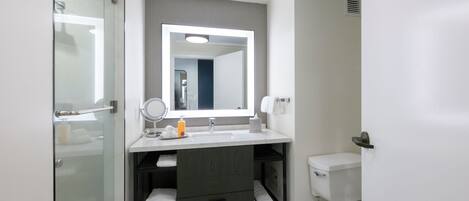 Un baño moderno con cabina de ducha de vidrio, un lavamanos blanco con un espejo grande y un inodoro.