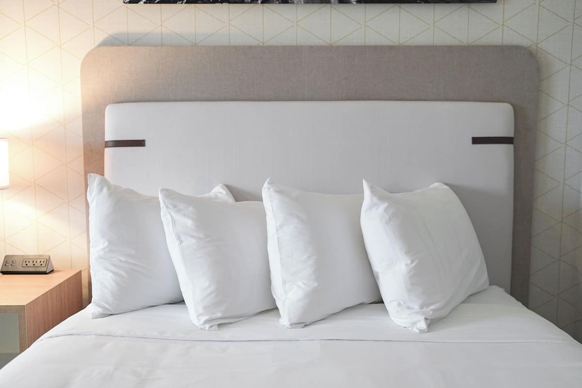A neatly made bed with a headboard, a bedside table with a power strip, and a wall with a geometric pattern.