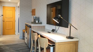 Cocina compacta con refrigerador integrado, una pequeña zona de comedor con dos sillas, una encimera y un televisor montado en la pared.