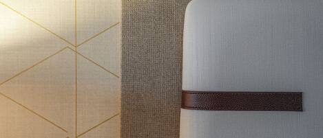 A close-up of a textured wall with a geometric pattern and a section of a grey upholstered headboard with a brown leather strap.