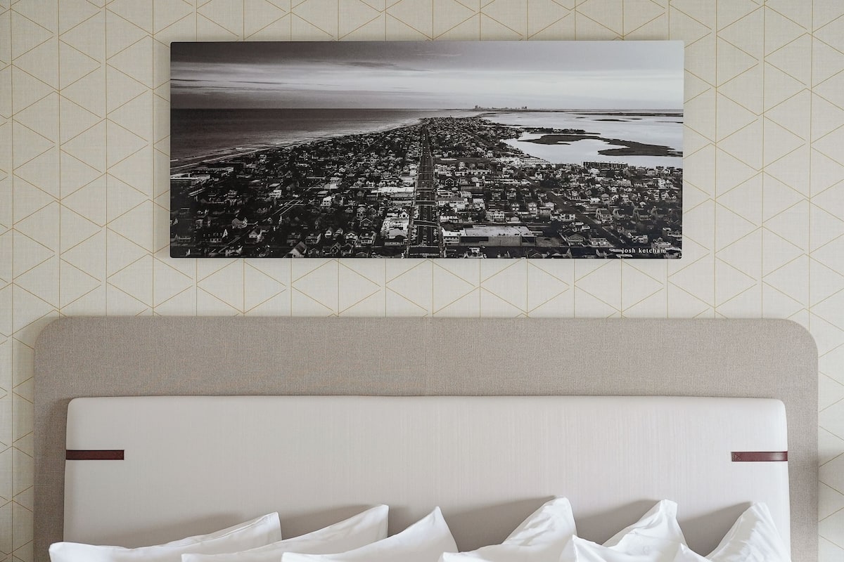 A bedroom with a large bed, a headboard, and a cityscape wall art.