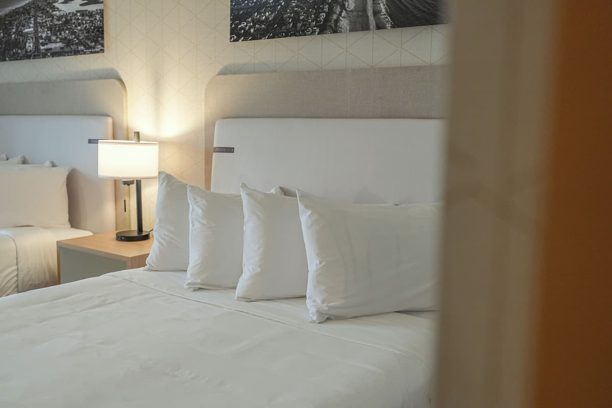 A hotel room with a large bed, a bedside table with a lamp, and a cityscape view on the wall.