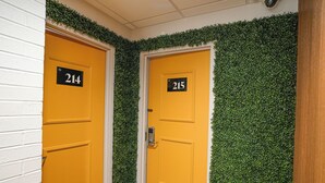 Dos puertas amarillas con números negros, 214 y 215, en un pasillo con paredes blancas y follaje verde.