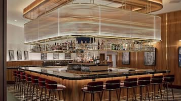 A bar area with a curved ceiling, multiple shelves of bottles, and red bar stools.