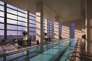 Une piscine intérieure moderne, dotée de grandes fenêtres, de chaises longues et offrant une vue sur le paysage urbain.