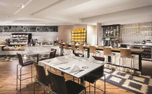 A modern restaurant with a bar area, marble tables, and a brick wall backdrop.