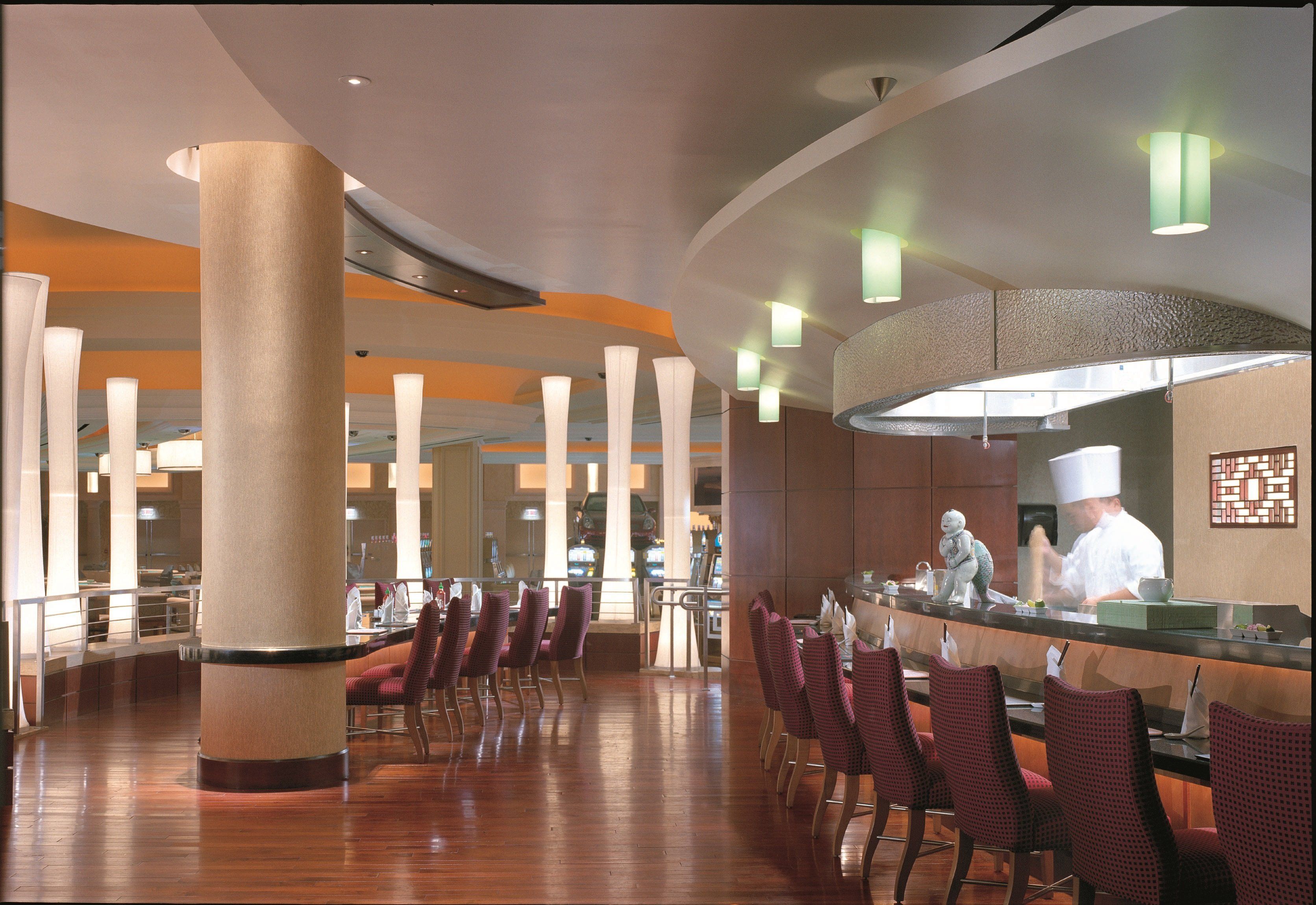 Um restaurante amplo, com pé direito alto, iluminação moderna e um bar central.
