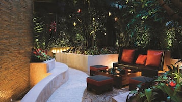 An outdoor seating area with a curved bench, a sofa, and a coffee table, surrounded by lush greenery and decorative lighting.